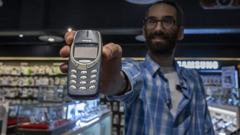 Homem segura um antigo telemóvel Nokia em uma loja de tecnologia, destacando-o em primeiro plano.